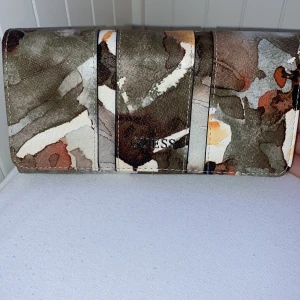 GUESS - It’s is a very unique purse due to the unique designs. It has of spaces in it which you can fit many things such as cards coins money or your phone!