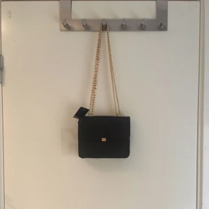  - Fin, svart väska med gulddetaljer! Köpt på Åhlens Aldrig använd! Prislappen sitter kvar! Nypris: 249kr. Mitt pris 150kr. Köparen står för frakten ✨