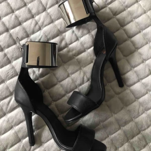  - Snygga klackar från Nelly. Svarta stilettklackar med stor silverdetalj runt ankeln. Dragkedja bak. Klackhöjd 10 cm. Ytterst lite slitna på få ställen. Knappt något som syns. 