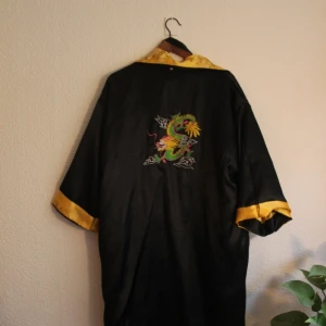 Vändbar kimono  - Sjukt fin vändbar vändbar kimono, storlek L. Men passar även större och mindre storlekar. Ena sidan är svart med en drake på ryggen. Och andra är gul med blommor och svarta detaljer. Frakt 44 kr 