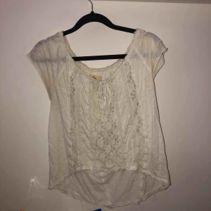 - Lätt och fin Hollister blus/ t-shirt. Enda märkbara på tröjan är att en av tofsarna på snörena är borta. Ingenting som är märkbart när man knyter ihop dem (se andra bilden).  Storlek: S Färg: Vit