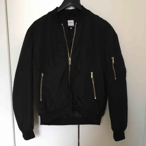  - Svart bomberjacka. Guldfärgade dragkedjor. Inköpt 2017. Använts under vår och sommar. Svaga vita märken på jackärm samt rygg, ev kommit till efter tvätt. Se bild 2. Hål i en av jackfickorna. Annars i fint skick! Kan mötas i Malmö, annars tillkommer frakt.