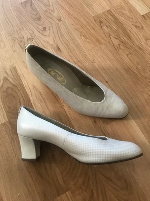 Scholl vita finskor - Vackra vita klackskor med små beige fyrkanter. Gulddetalj bakpå. Från Scholl, mycket bra kvalitet, tror de heter Jasmine. Står stl 6, vilket är stl 39. Välbehållen klack då skorna knappt har använts. 