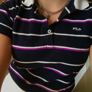 Fila pikétröja - Fila pikétröja köpt på secondhand i Köpenhamn några år sen. Mörkblå med vita och lila ränder. Har inte kommit till användning därför säljer jag den