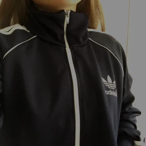 Adidas kofta - Säljer denna fina mörkblåa koftan då jag ej har någon användning för den längre.Det finns en ficka på varje sida, ett litet tryck på ena sidan på framsidan & ett stort tryck på baksidan. Skicket är väldigt bra! 