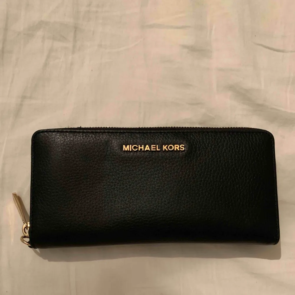 Svart clutch/plånbok från Michael Kors med guldiga detaljer! Använd 1 gång. Kan användas som antingen en mindre clutch eller en större plånbok då den har plats för mobil samt fickor och korthållare etc. Nyskick!. Väskor.