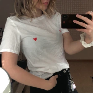 Vit t-shirt med detalj  - En fin vit t-shirt med två hjärtan på vardera bröst och tröjan har därpå aldrig blivit buren vilket innebär att den är i således bra skick. Frakt ingår inte