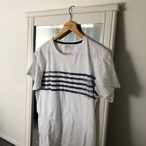 Vit t-shirt  - Vit t-shirt med blåa ränder i storlek L (man storlek). Använt ett par gånger, fortfarande i bra skicka Frakt förekommer, men kan mötas i Göteborg. För fler frågor och bilder kontakta mig! 