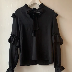 Svart blus - En svart blus med rosette på halsen. Knappt använd. Ordinarepris 199kr säljes för 50kr + frakt. Storlek 36
