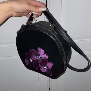 Oanvänd väska med 3 st jättefina lila färgade blommor. Väskan är justerbar finns ett långt band man kan justera och ett kort, man kan ta bort de långa med hjälp av axelbandsrem 