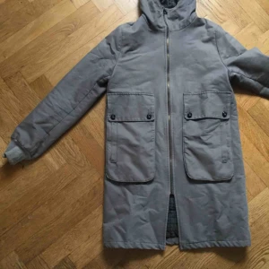  -  Fin och varm jacka från Bric-a-brac, stilren grå med rutigt foder. Begagnat skick, några små slitningar- se bild två. Kan skicka fler bilder om önskas. Upphämtas i Stockholm Hägersten. Kan även mötas upp. Vid frakt står köpare för frakten! 