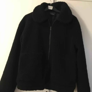 Svart teddyjacka - Svart teddyjacka med krage och stora fickor framtill. Mudd i nederkant och vid ärmslut  Finns i Linköping eller skickas mot fraktkostnad🌸