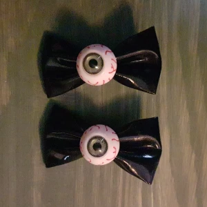 Hårspännen med rosetter och ögon  - Två hårspännen med svarta rosetter och ögon m. ådror, iris i ögonen är grön. Frakt tillkommer.