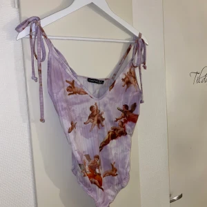Body med änglar  - Jättefin body med änglar på som jag beställde från Asos (från boohoo) när jag var i Australien. Aldrig använd vara testad så är oanvänd. I storlek M men eftersom man kan justera axlarna så skulle jag säga att det är en flexibel storlek. Säljer denna för 160kr (FRAKT INGÅR). Fler bilder går att få om man är intresserad :) flera är intresserade så högsta bud vinner 🌞 