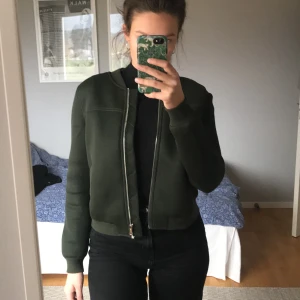 Vadderad militärgrön jacka - En vadderad militärgrön bomberliknandejacka. Hyffsat varm. Den kommer tyvärr inte till använding :( köptes i USA för några år sedan och har använts en gång. Färgen på sista bilden stämmer inte överens med den verkligheten.