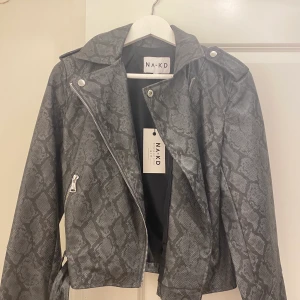 Skinnjacka med orm mönster  - Jätte fin skinnjacka i grått med ormmönster i strl M men passar bra till både S och M köpt på nakd och prislappen är kvar på den så aldrig använd 