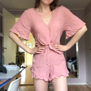 River Island rosa jumpsuit - Rosa jumpsuit från River Island. Använd ett fåtal gånger. Är egentligen lite för stor för mig. Egentligen inte så skrynklig, stryks den blir den ännu finare!