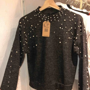  - Grå tröja i mjukt material med pärlor över bröstet längst armarna. Köpt utomlands därav storleksskillnaden. Aldrog använd 