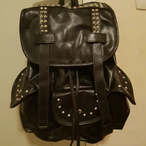  - Svart fusk skinn ryggsäck med nitar. Rymlig väska med ett stort fack och tre mindre. Vadderad rygg så perfekt för böcker och laptop.  Eventuell fraktkostnad tillkommer.