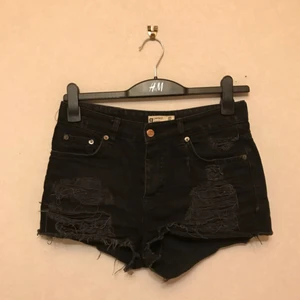  - Svarta jeansshorts från Gina Tricot, storlek 38. Fabriksgjorda slitningar på framsida och baksida. Knappar istället för dragkedja i gylfen. Hög midja. Frakt tillkommer!