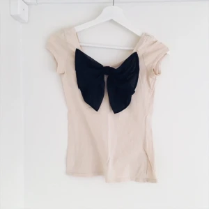  - Beige t-shirt med en svart rosett, rosetten är i transparent material. Från H&M, stor i storleken 