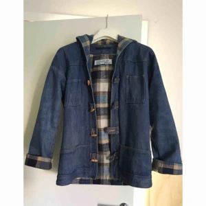  - Riktigt cool jeansjacka med rutigt innefoder. Huva och knäppning istället för dragkedja.  Katt finns i hem, köpare betalar frakt om de ska skickas. Kan annars mötas upp i Göteborg/Partille. 