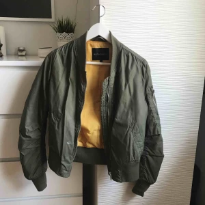  - Bomber jacka i militärgrönt med gul insida! Bekväm jacka! Passar bra till våren men även sommaren. Väl använd men fortfarande fin.  Det finns två färgfläckar på jackan (visas på bild tre)