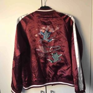  - Jätte fin bomberjacka i vinrött och vitt med ett print på ryggen! Lagom fodrad, bra som vårjacka! Har 2 fickor fram och dragkedja i mitten! Knappt använd, jätte fint skick, som ny! Passar säkert storlek M också. 