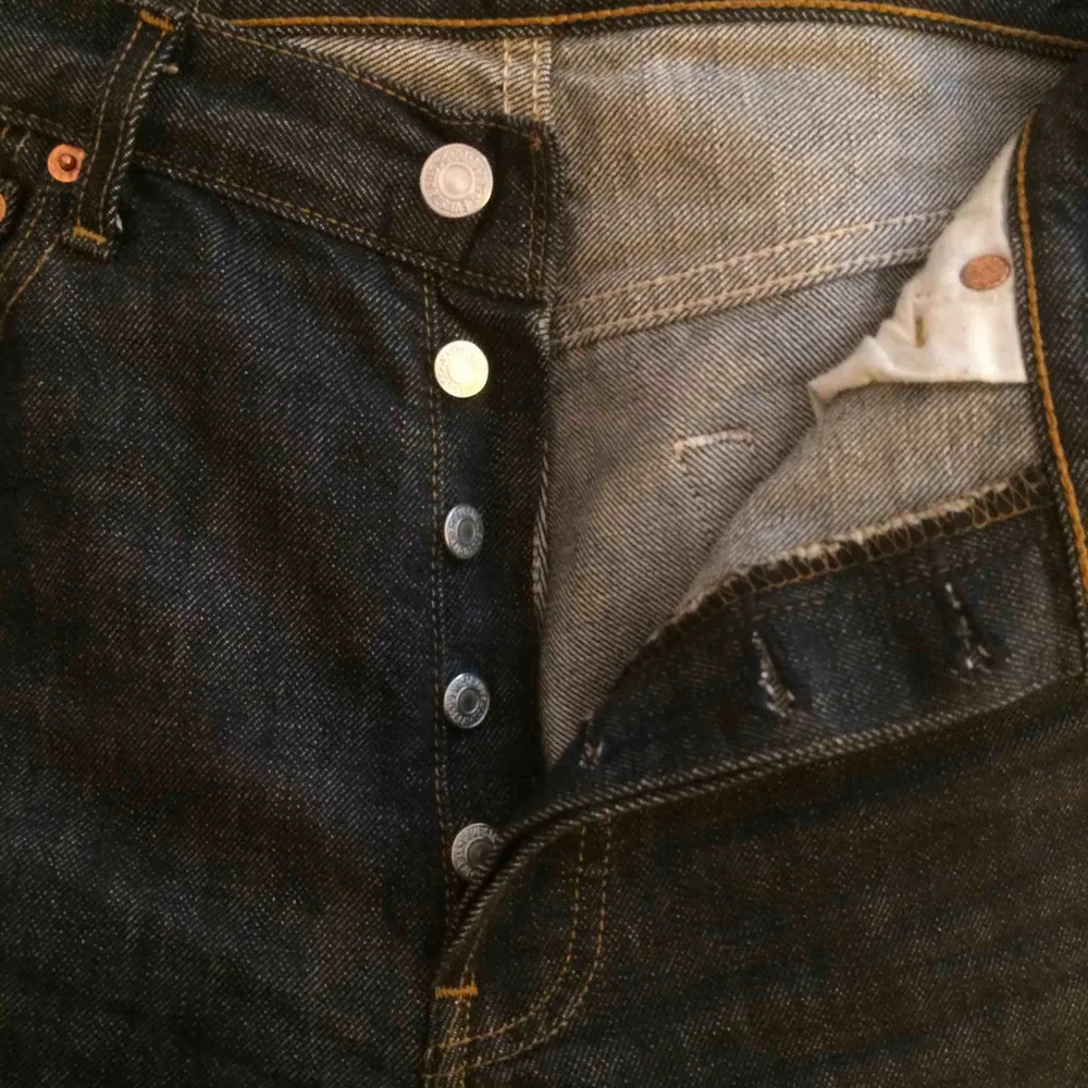 Ett par mörk blågråa Levi’s jeans med knappar i stället för gylf, väldigt bra skick med rough cut i byxben slutet. Jeans & Byxor.