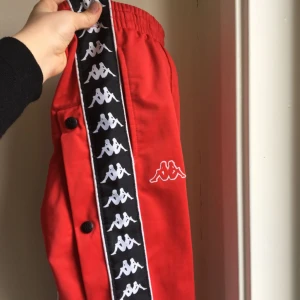  - Röda kappa byxor med knappar längst bena. Stl S. Använt väldigt sparsamt. Köparen står för frakt. 