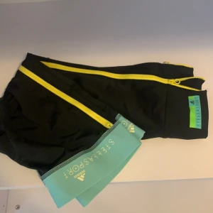 Adidas, Svarta träningstights - Adidas samarbete med Stella Mcartnys sportkläder, passar perfekt som yogabyxor/ pw byxor. Gul dragkedja längs hela sidorna // Frakt tillkommer!💗