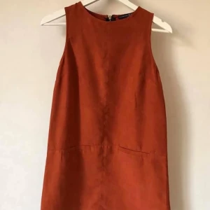 Roströd mockaklänning, 34-36 - Röd klänning i tunnare mocka-liknande tyg. Fodrad inuti med skönt sidenliknande material. Oanvänd! Strl 10. Dvs 34-38?  Kan mötas i Stockholm eller skicka mot fraktkostnad! ✨🌸✨