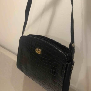  - Superfin svart väska i lite glansigt ormskinnsmatrial och gulddetaljer! Banden är justerbara!