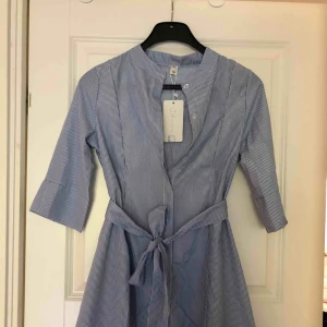  - Helt ny kort, blåvit skjortklänning med knytband. Prislapp hänger fortfarande kvar. Hämtas i Malmö eller skickas mot frakt. 