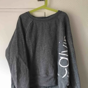  - En grå hoodie utan luva från Calvin Klein med text på sidan (andra bilden) storlek S, (frakten är inte inkluderad i priset)  
