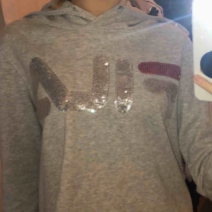  - En grå hoodie med glitterdetaljer (det står FILA)