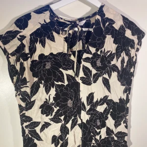 Mönstrad blus - Svart vit mönstrad blommig blus. Skönt runt material så perfekt på sommaren. Super söt knytdetalj vid bröstet. Strlk 38 men passar typ Xs-M