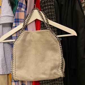 Grå/silvrig väska, lik stella mccartney - Liten grå och silvrig väska i bra skick. Väldigt snygg men kommer inte till användning. Frakt tillkommer. Skriv om ni har några frågor. Kan mötas upp i Lund 🌸🤍🌈🍒🐬