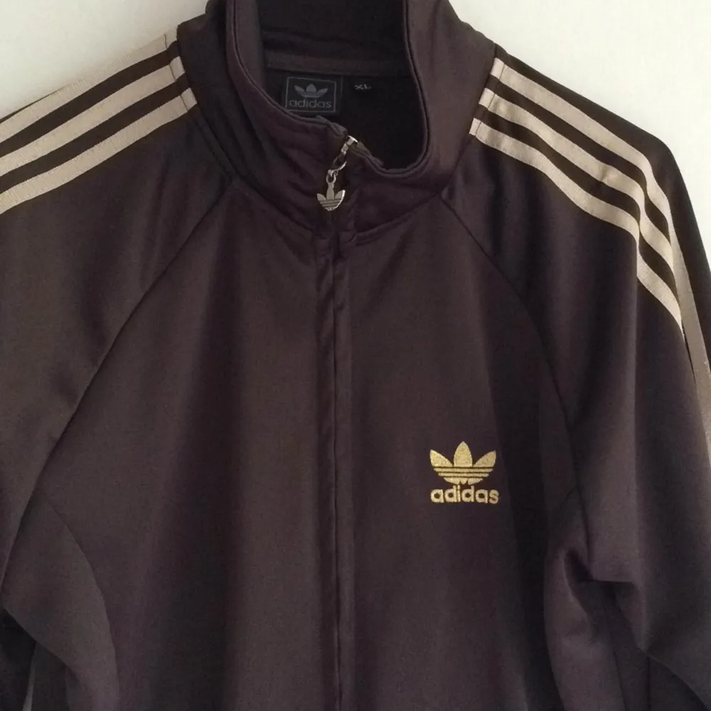 Mörkbrun adidas med guldiga ränder på armarna. Med dragkedja. 
Strl XL men skulle mer säga att det är en s eller m.. Hoodies.