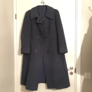  - En lång kappa ner till strax ovanför knäna. Tyget är typ tovat med färgen mörkblå. Kappan har otroligt mycket struktur och är en perfekt varm vinterjacka. Den har superfina detaljer vid ärmen och vid fickan (se tredje bild)!!!!! Kan mötas var som helst i Stockholm och Dalarna