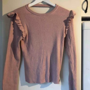  - En långärmad rosa tröja, volanger på axlarna, lite öppet i nacken! Skickas ej