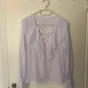  - Vit transparent blus med knytbara band i v-ringning samt volang längst ned på ärmen. Aldrig använd. 