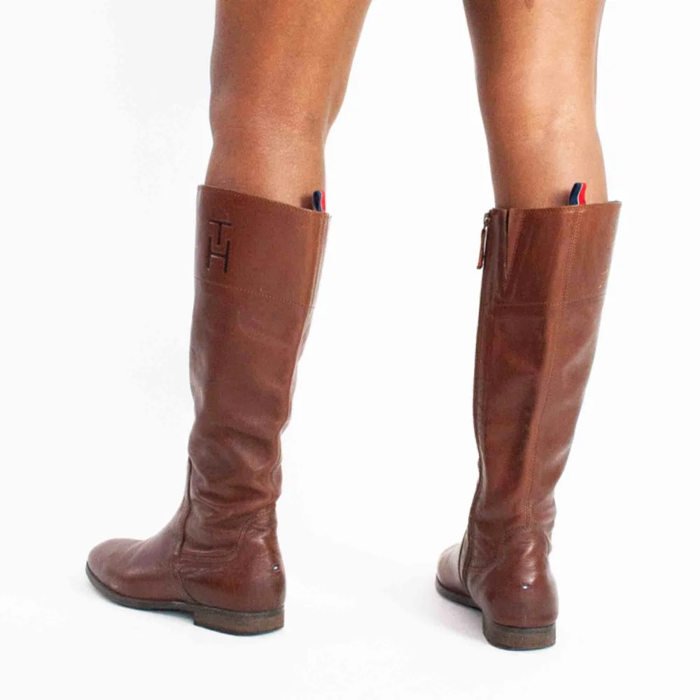 Tommy Hilfiger knee high real leather boots in brown size 39 A visible scratch on the right shoe, no anti slippery protection SIZE Label: 39 EU, feels like true to size Model: 169/39 (shoes) Measurements: Foot: 27 cm Ankle: 29 cm Shin: 40 cm Height: 41 cm. Skor.