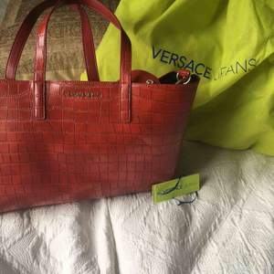 En äkta Versace väska ( med authenticity tag)  i imitations läder knappt använd och med löstagbar bagstrap samt en ”inneväska” som går att ta bort