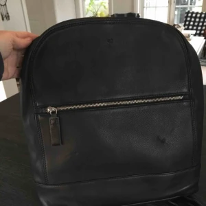 Ryggsäck skinn - Skinnryggsäck ”Ruby”. Fack med dragkedja på framsidan. Vadderat fack för dator i stora facket. Smart fack med dragkedja på baksidan. Mått ca 31x37x7 cm. Mkt fint skick. Llitet ”tryckmärke” på framsidan. Nypris ca 2000:-. Frakt betalas av köparen. 